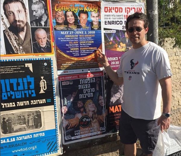 avi liberman pointing at a an ad for comedy for koby