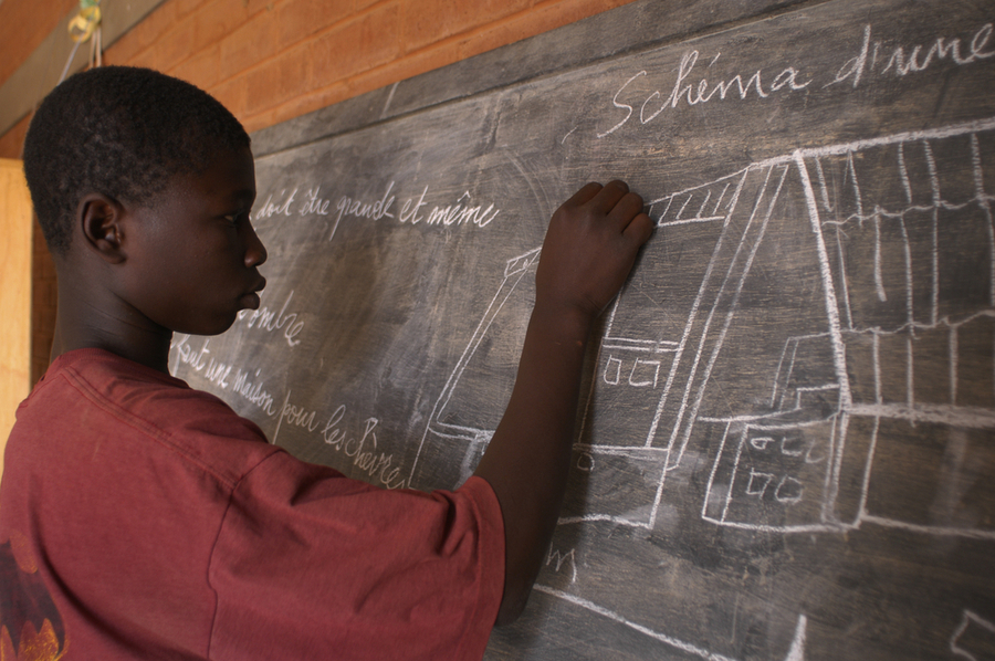 An African teenager solving a math question in a blackboard linked to university of the people