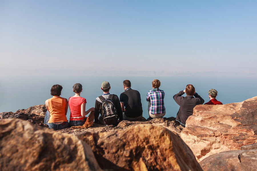 a group of travelers sitting by the view of the dead sea on the mountains